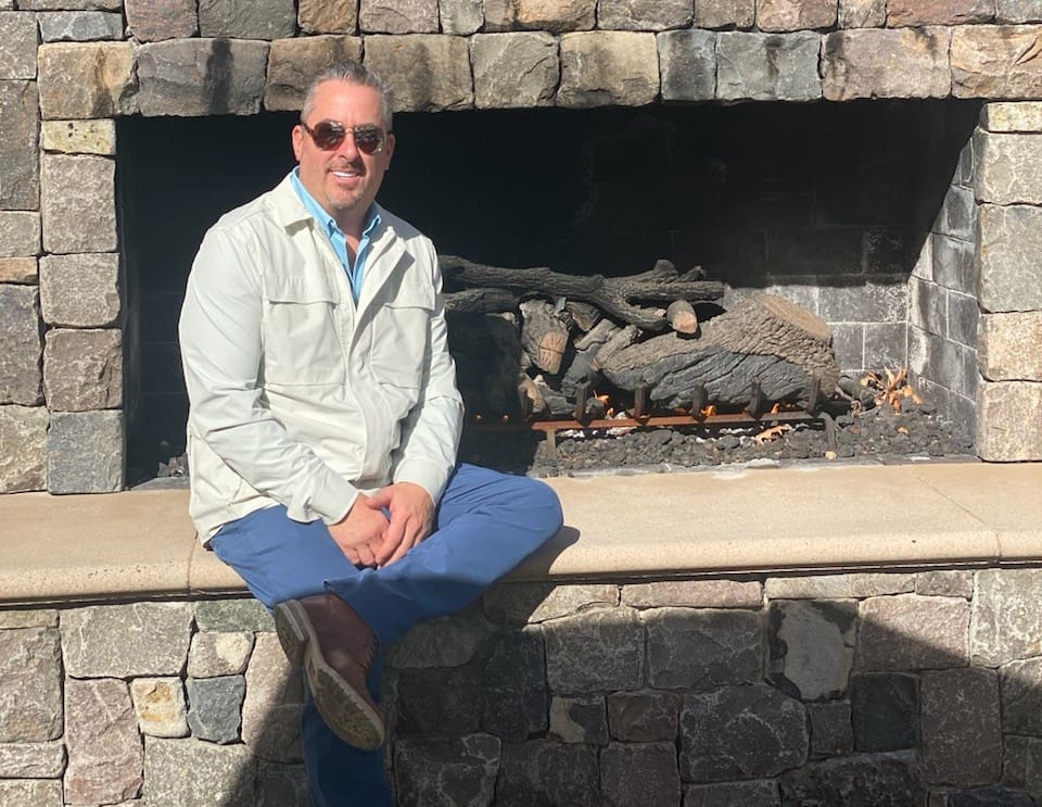 A man sitting on the edge of a stone fireplace.